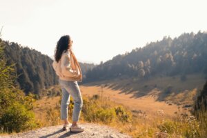 a-woman-standing-on-top-of-a-hill-next-to-a-forest