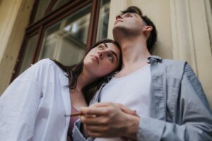 A couple leans affectionately on a balcony, gazing upwards in a relaxed outdoor setting